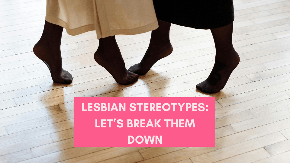 Close-up of two people standing barefoot on a wooden floor, facing each other, with the text 'Lesbian Stereotypes: Let’s Break Them Down' in bold pink letters.