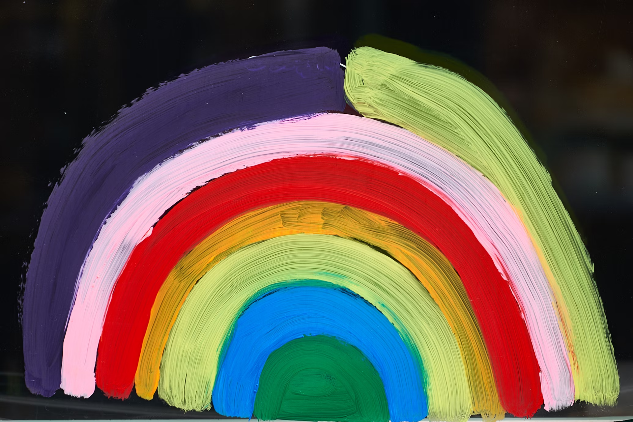 Hand-painted rainbow with textured brushstrokes on a glass surface, symbolizing queer pride.